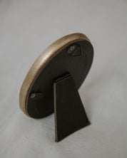 Small round wooden object with a black stand on a gray background
