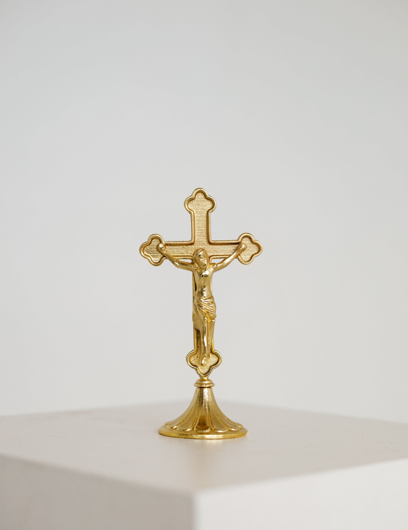 Small gold standing crucifix on a footed base, shown on a white background, modern Catholic home decor.