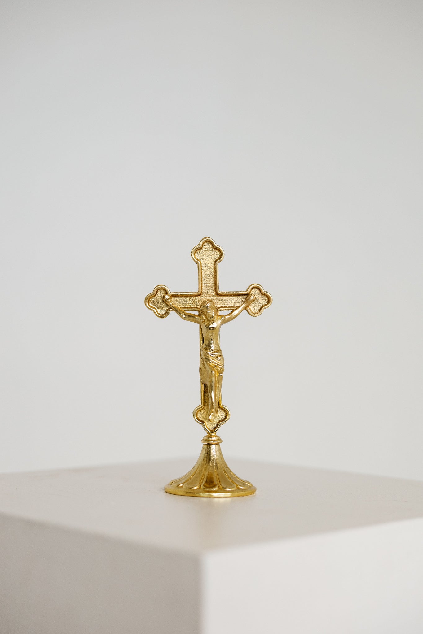 Small gold standing crucifix on a footed base, shown on a white background, modern Catholic home decor.