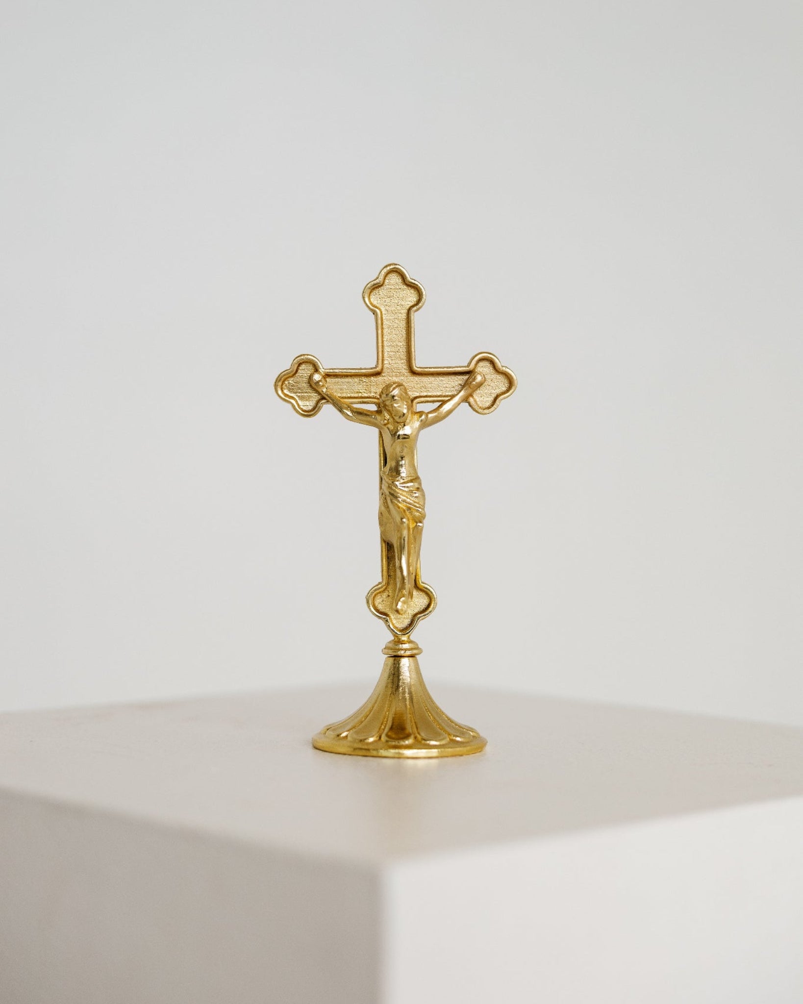 Small gold standing crucifix on a footed base, shown on a white background, modern Catholic home decor.