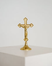 Small gold standing crucifix on a footed base, shown on a white background, modern Catholic home decor.