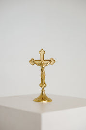 Small gold standing crucifix on a footed base, shown on a white background, modern Catholic home decor.