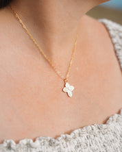 Gold necklace with a four-way cross styled on a person wearing a light gray top.
