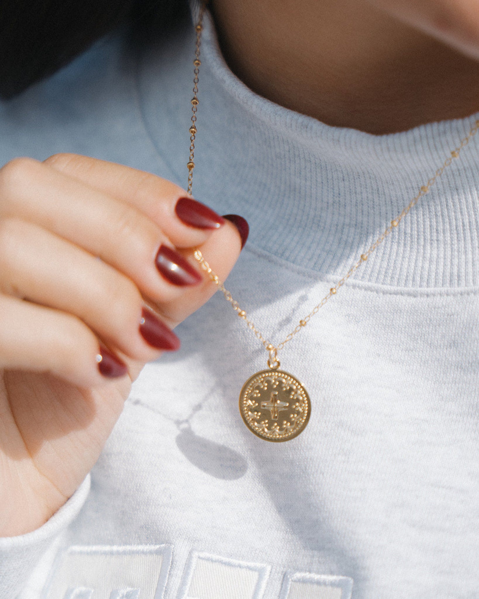Gold necklace with a round pendant worn by a person against a light background