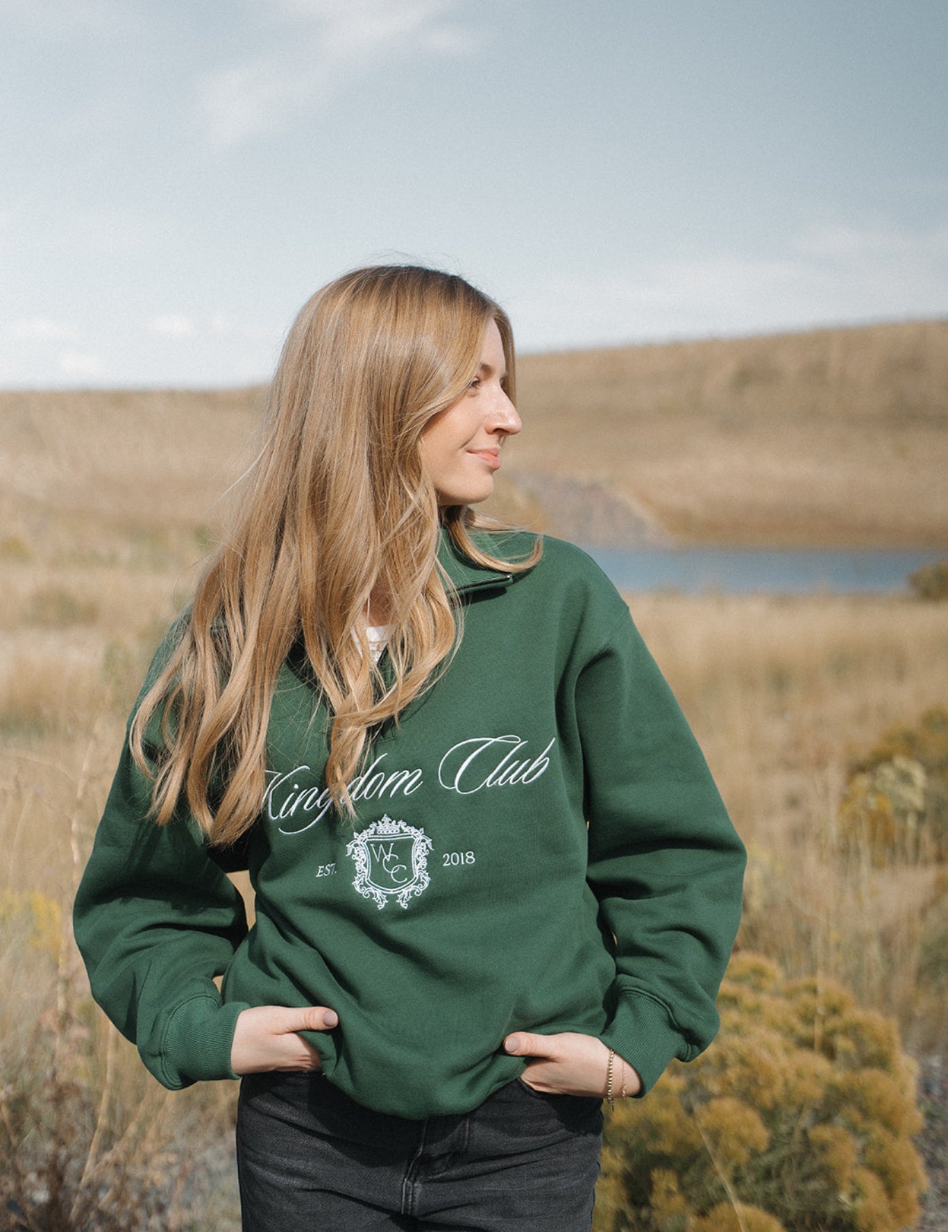 Person wearing a green 'Kingdom Club' sweatshirt in a natural setting