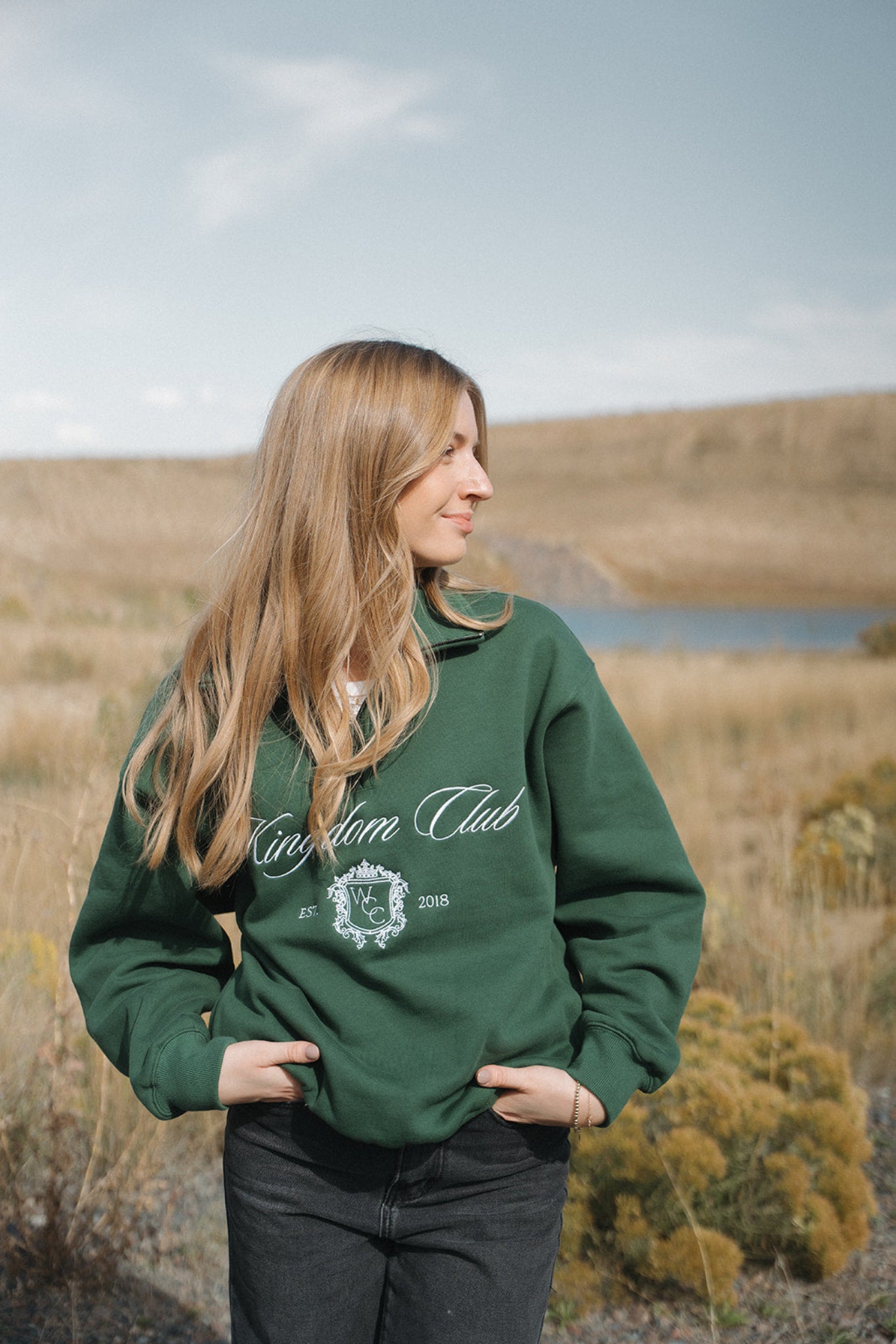 Person wearing a green 'Kingdom Club' sweatshirt in a natural setting
