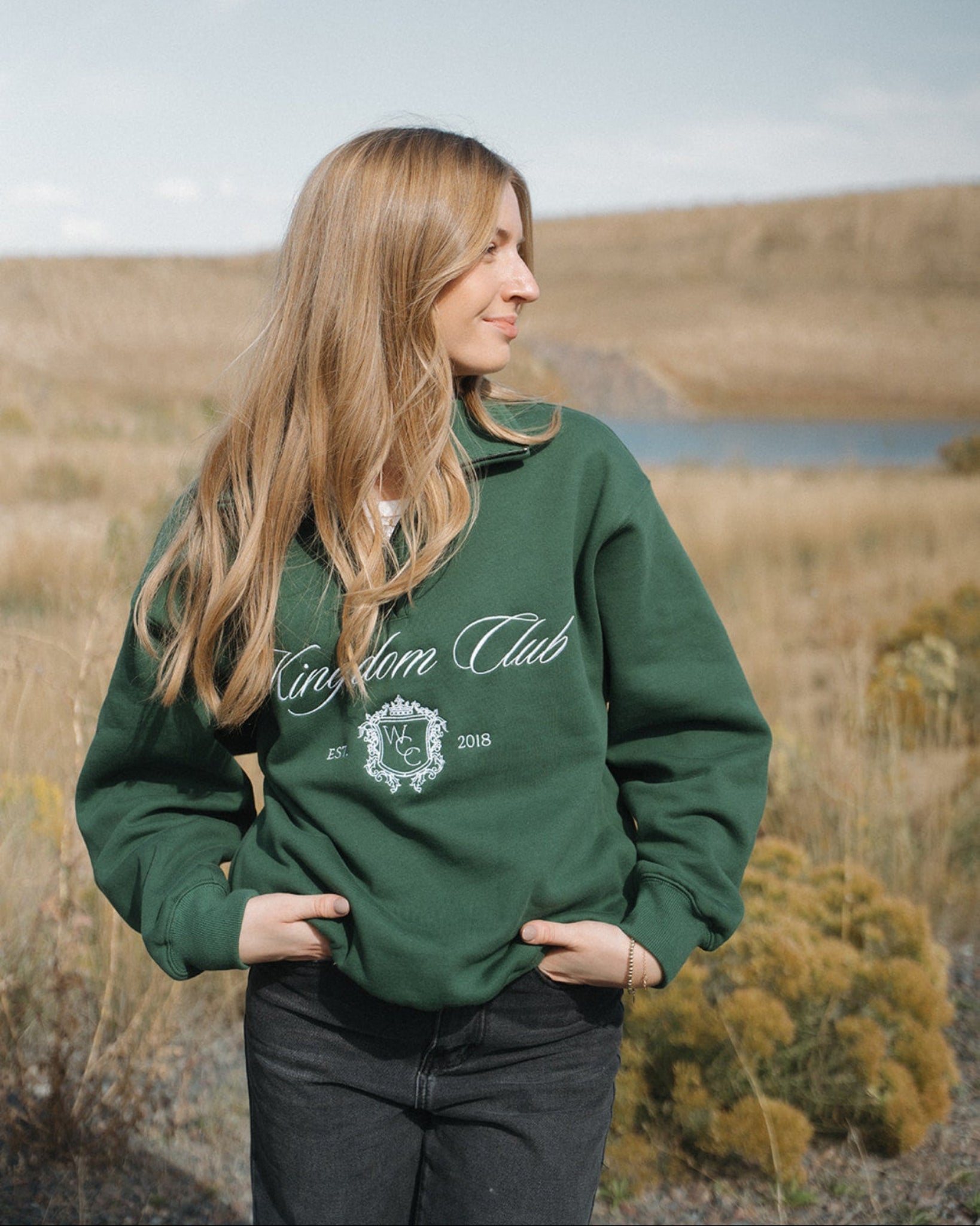 Person wearing a green 'Kingdom Club' sweatshirt in a natural setting
