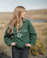 Person wearing a green 'Kingdom Club' sweatshirt in a natural setting