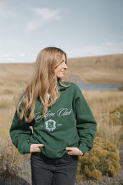 Person wearing a green 'Kingdom Club' sweatshirt in a natural setting