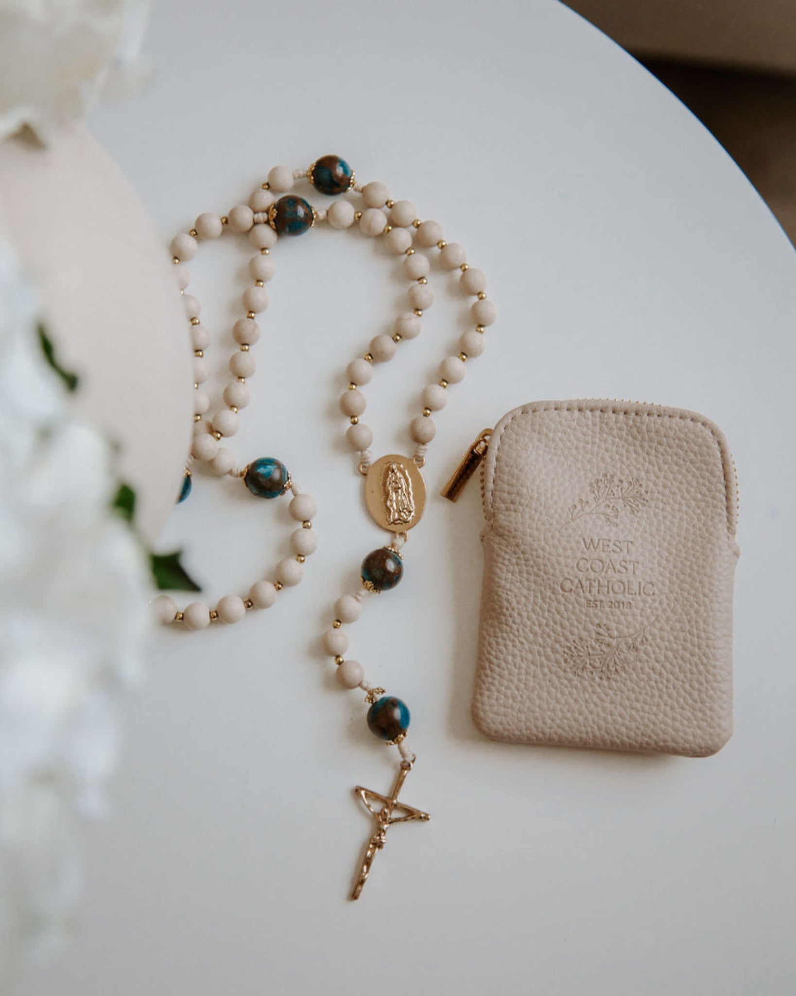 Rosary and beige pouch on a white surface with blurred background