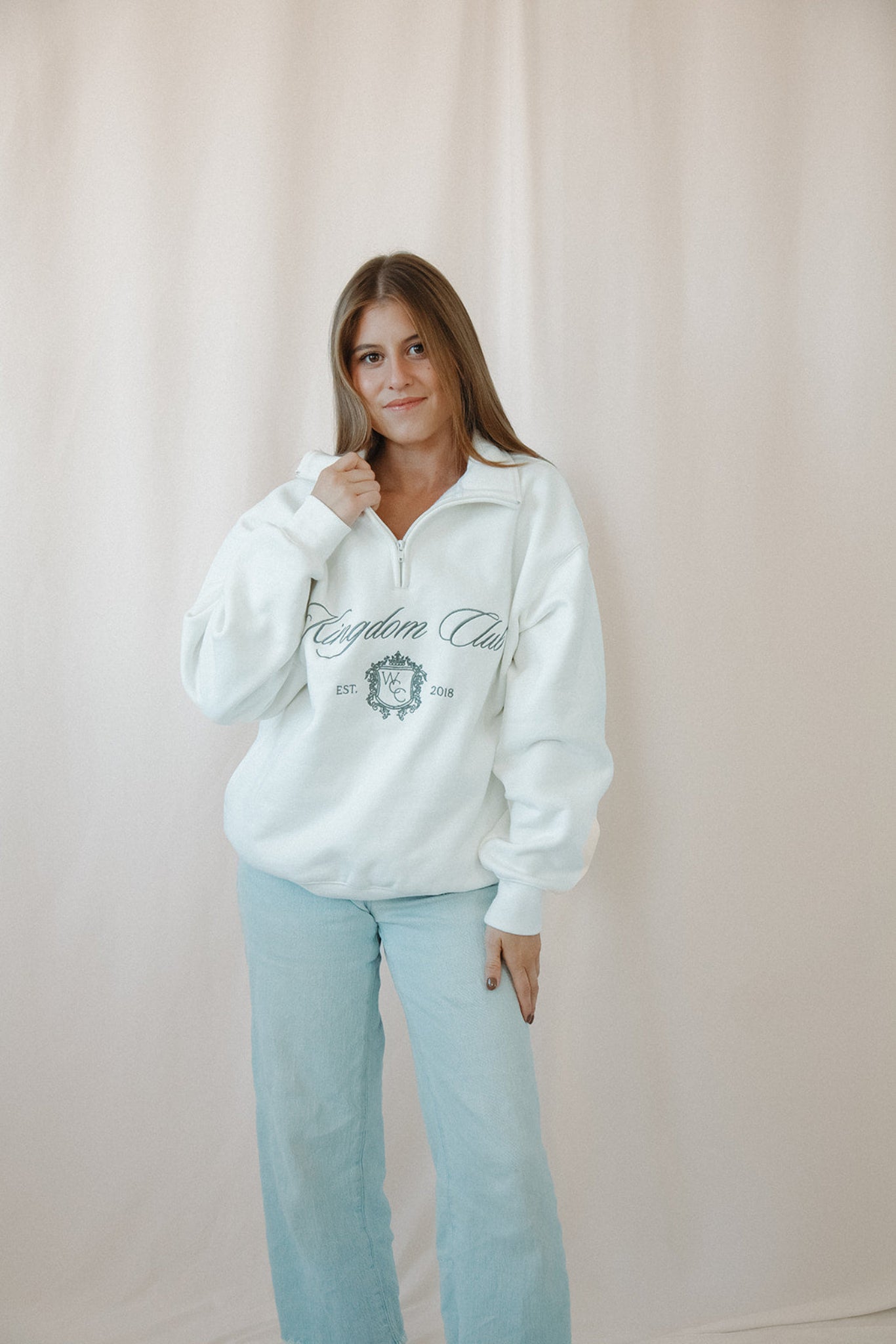 Woman wearing a white catholic sweatshirt with text and graphics, standing against a plain background