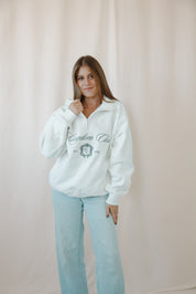 Woman wearing a white catholic sweatshirt with text and graphics, standing against a plain background