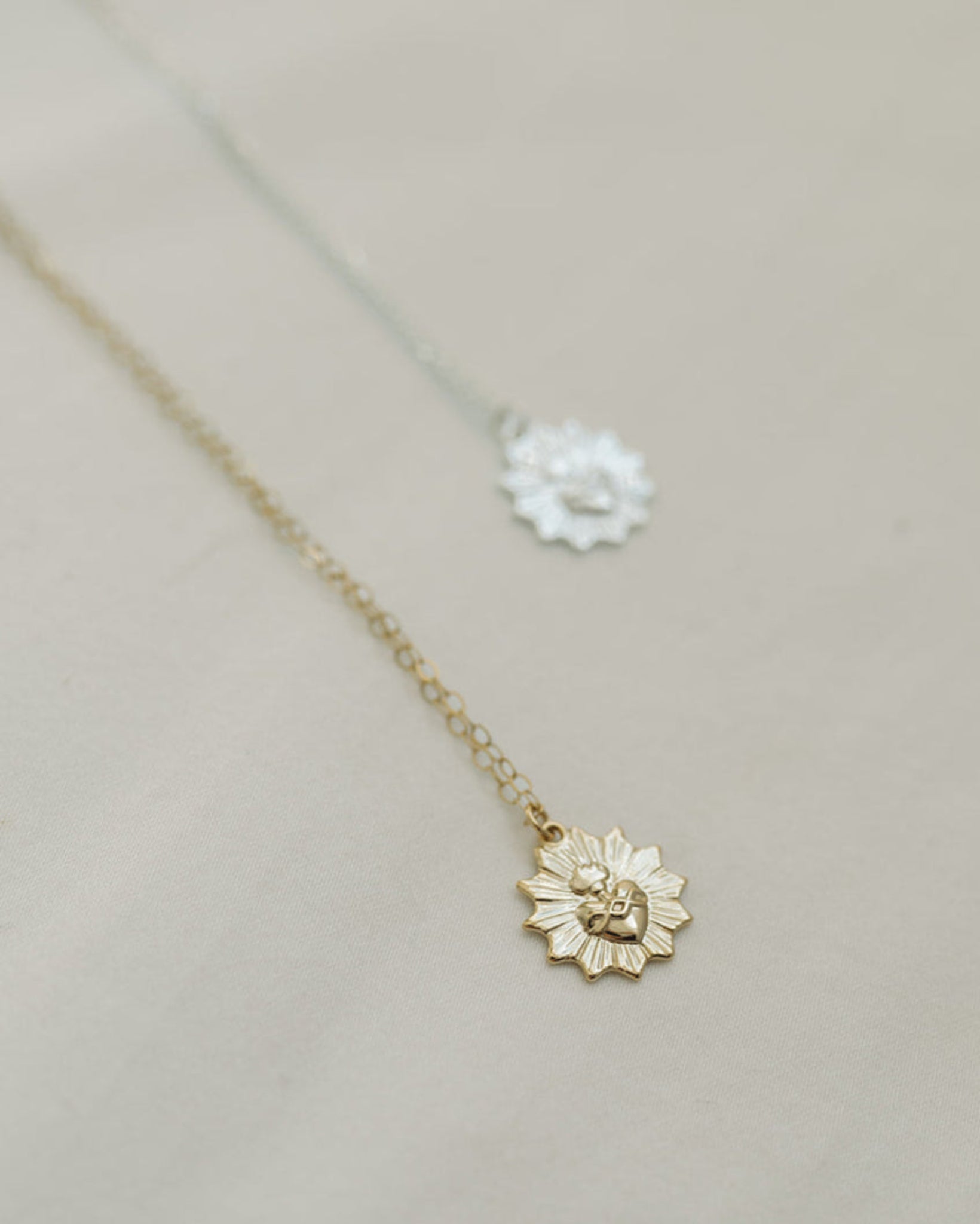 Two necklaces with a sacred heart charm one is gold and one is silver.