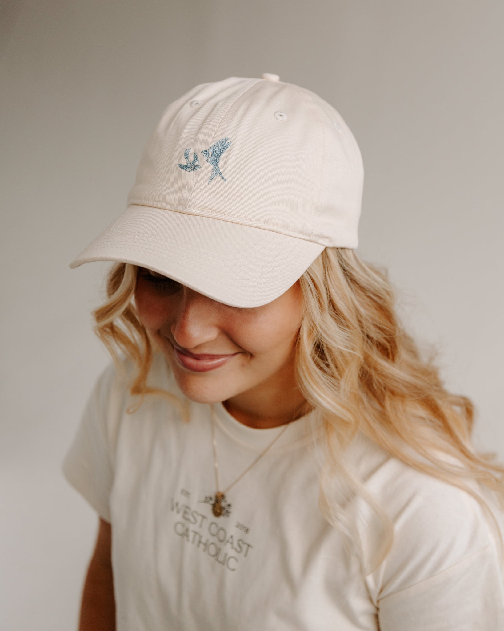 Woman wearing a beige cap with blue swallows and t-shirt with text on a plain background