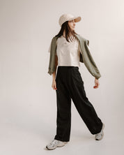Person wearing a beige shirt, green jacket, black pants, and white sneakers on a white background