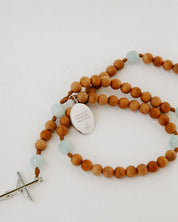 Wooden rosary with light blue beads and a silver cross on a white background
