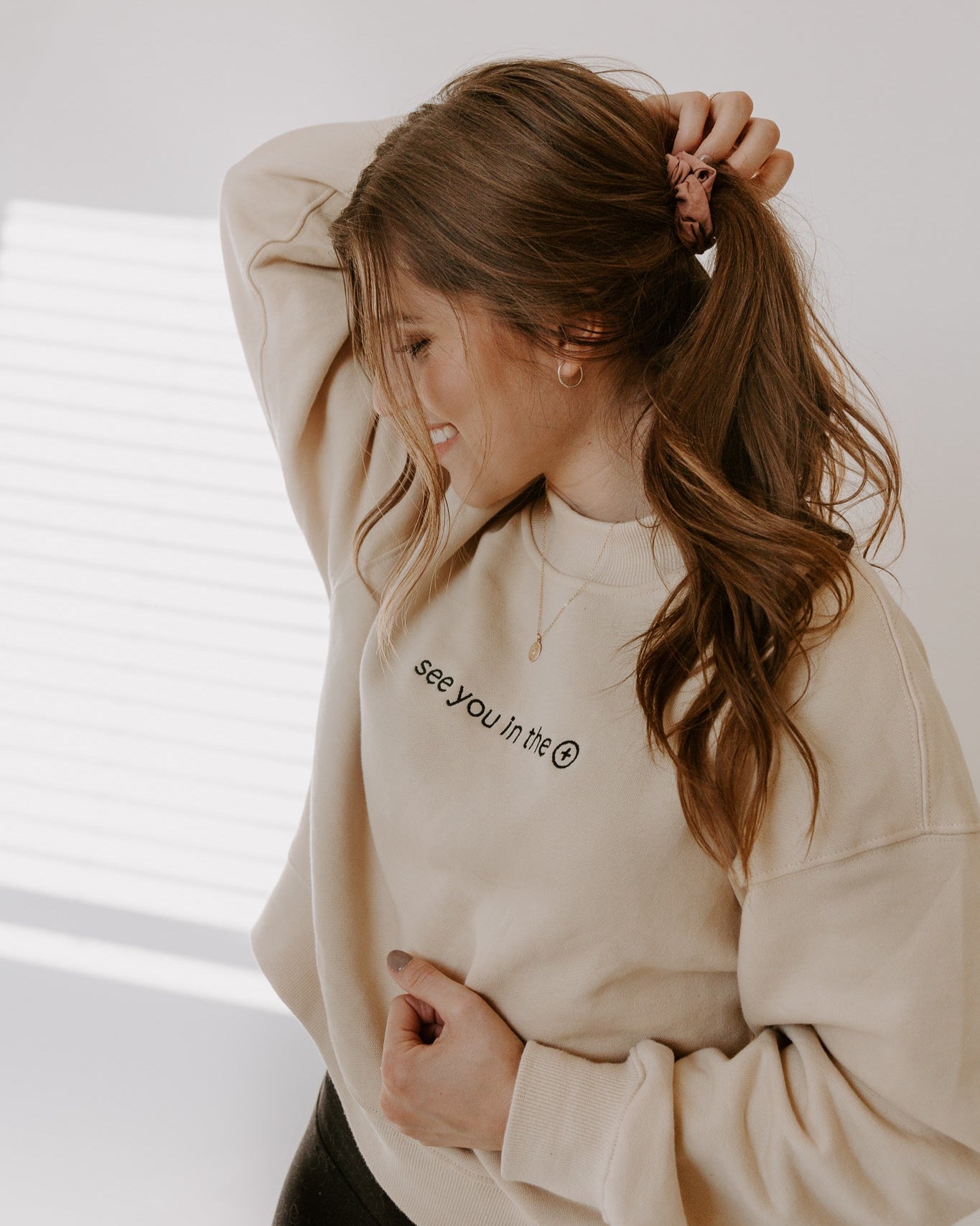 Woman wearing a beige sweatshirt with text, standing against a neutral background