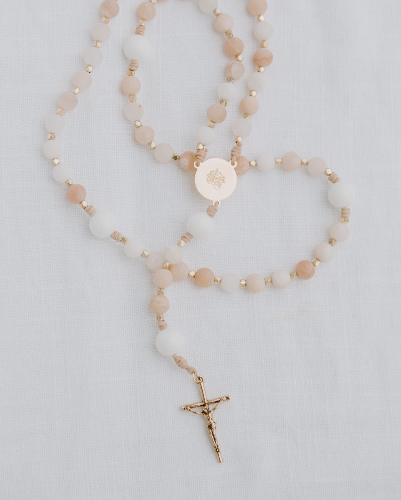 Pink and white immaculate heart rosary with gold medal on white background