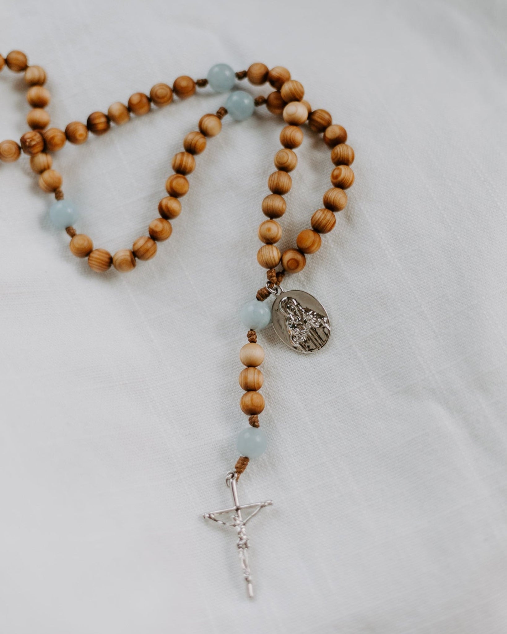 Wooden rosary with blue beads and a silver cross on a light gray background