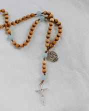 Wooden rosary with blue beads and a silver cross on a light gray background